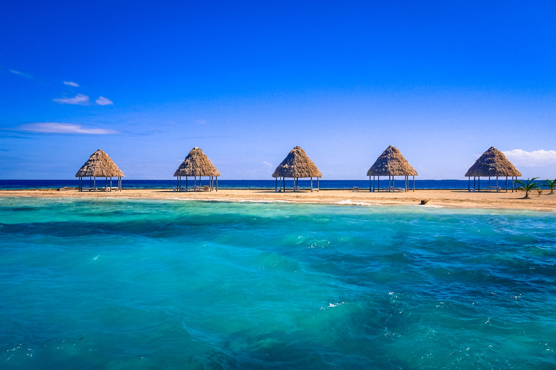 Thatched palapas on the golden sands of Rendezvous Caye in the Belize Barrier Reef.