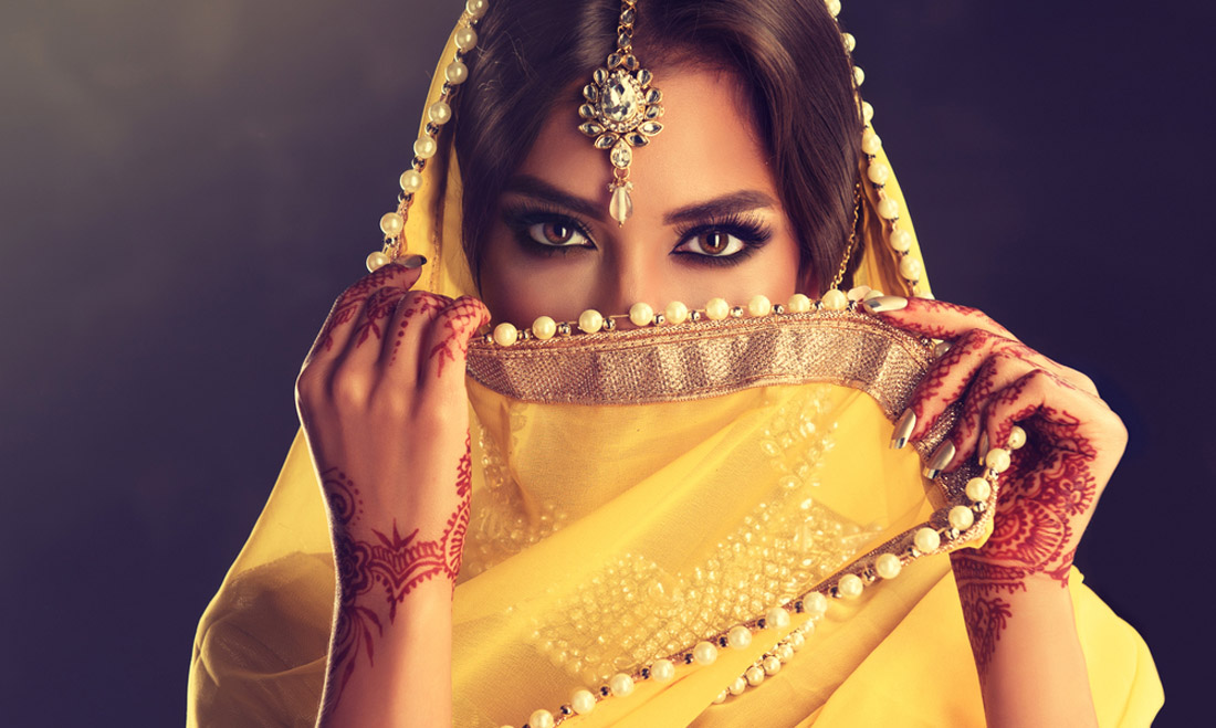 Indian woman in yellow saree, adorned with kundan jewelry and mehndi tattoo.